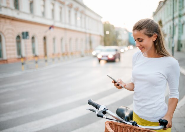 Moça bonita com uma bicicleta usando um telefone na cidade.