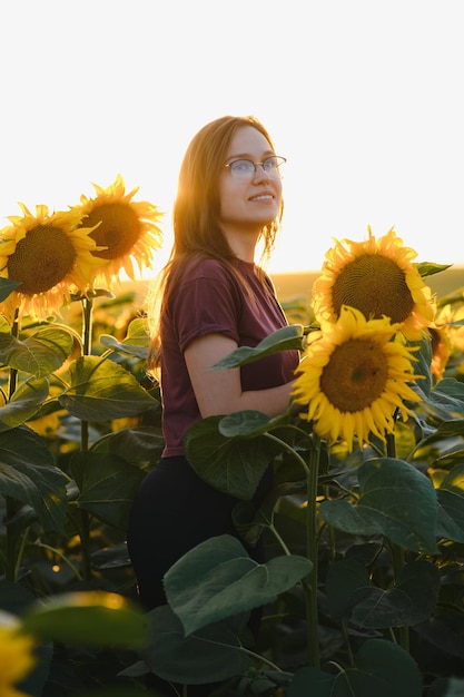 Moça bonita que aprecia a natureza no campo dos girassóis no por do sol