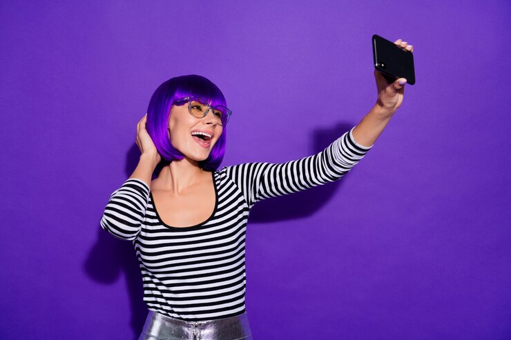 Foto moça bonita segurando telefone tirando selfies falando skype melhor amiga usar especificações pulôver listrado isolado fundo roxo