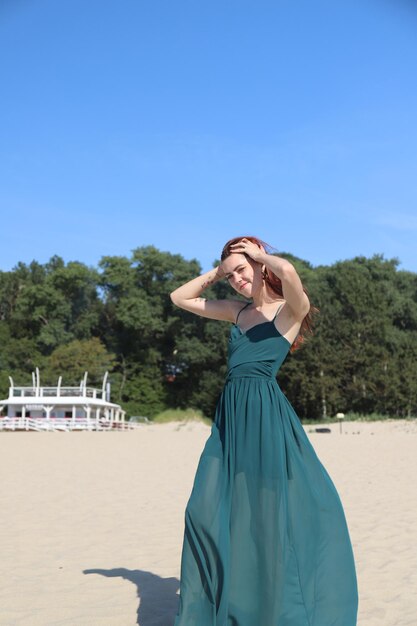 Moça com cabelo vermelho no vestido verde na praia