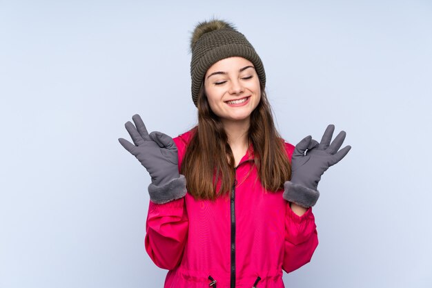 Moça com chapéu do inverno na parede azul na pose do zen