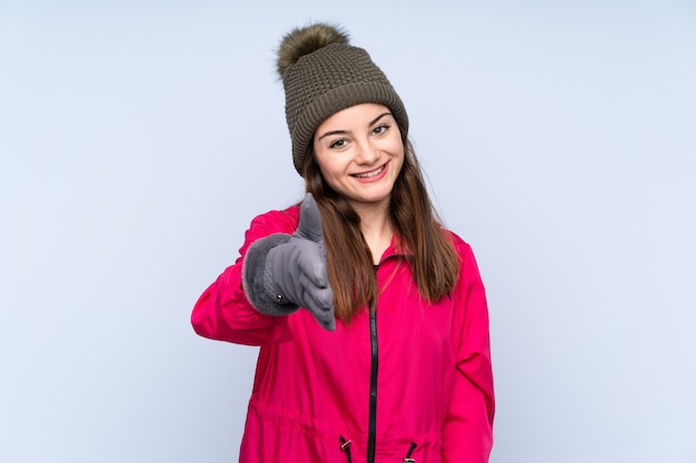 Moça com chapéu do inverno na parede azul que agita as mãos para fechar bastante