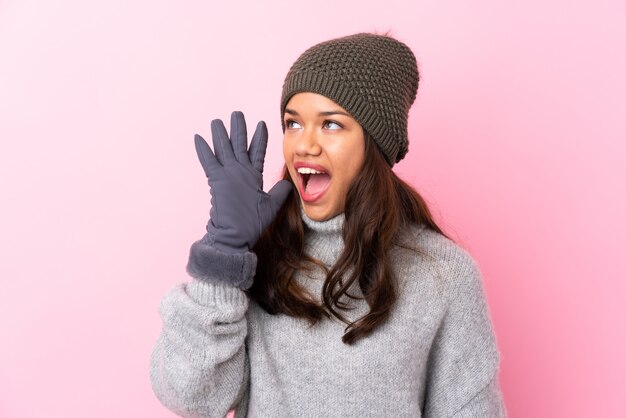 Moça com chapéu do inverno sobre a parede cor-de-rosa que grita com a boca aberta