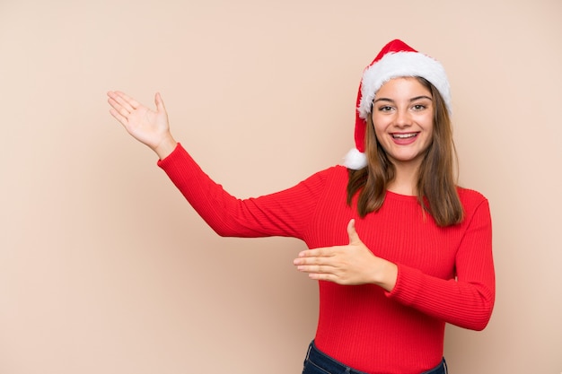 Moça com chapéu do Natal sobre a parede isolada que estende as mãos ao lado para convidar a vir