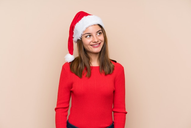 Moça com chapéu do Natal sobre a parede isolada que ri e que olha acima