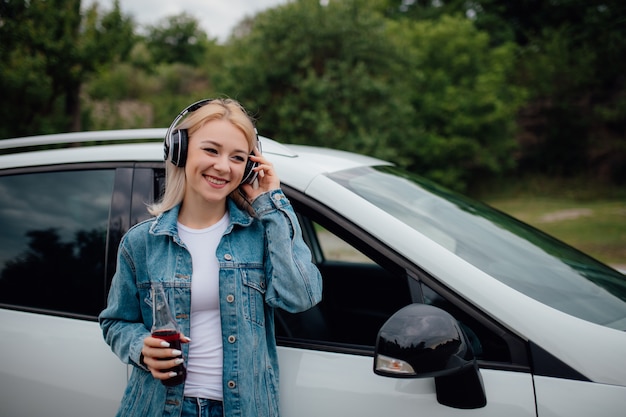 Moça com fones de ouvido, ouvindo música ao lado do carro