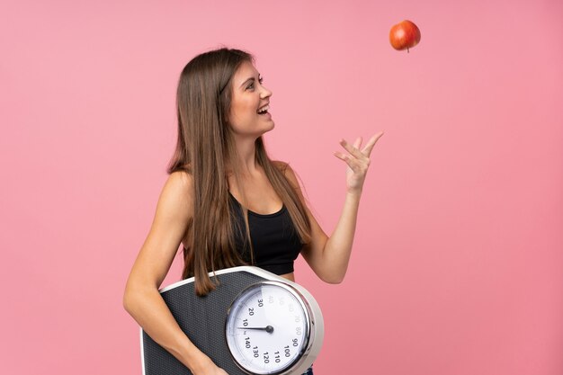 Foto moça com máquina de pesagem e com uma maçã sobre a parede rosa isolada