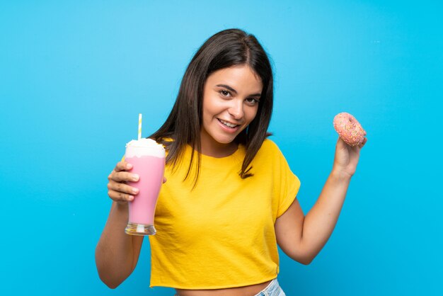 Moça com milk-shake de morango e um donut sobre parede azul isolada