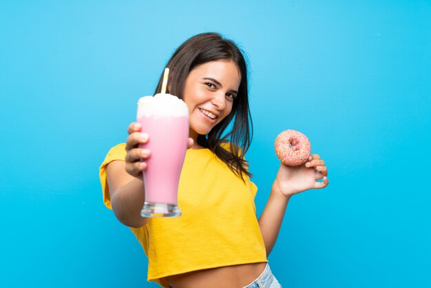 Moça com milk-shake de morango e uma rosquinha sobre parede azul isolada