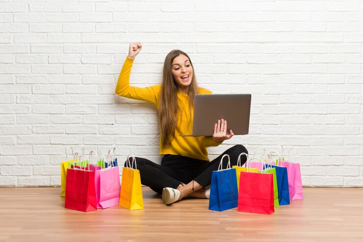 Foto moça com muitos sacos de compras com laptop e comemorando uma vitória