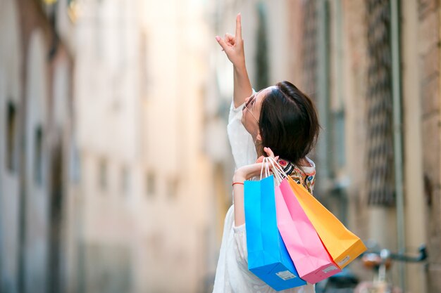 Moça com os sacos de compras na rua estreita na europa. retrato de uma linda mulher feliz segurando sacolas sorrindo