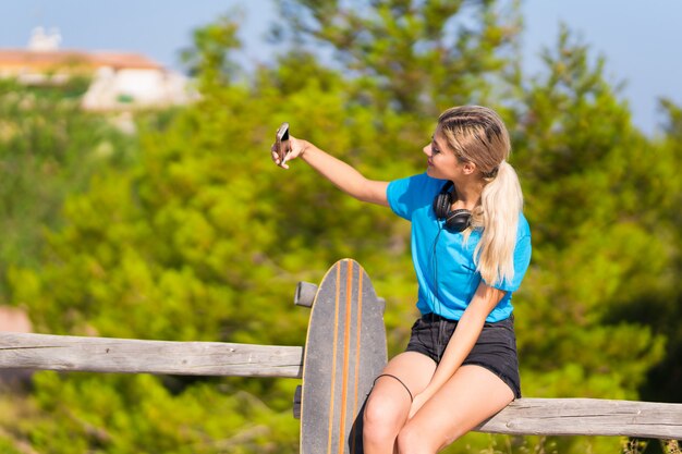 Moça com skate ao ar livre, tomando uma selfie com o celular