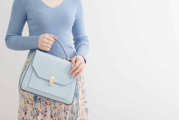 Moça de blusa azul e saia plissada com bolsa azul sobre fundo branco