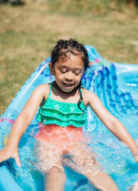 Moça de raça mista em casa a divertir-se num dia quente de verão na piscina infantil.