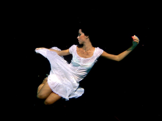 Moça debaixo d'água na piscina com vestido branco