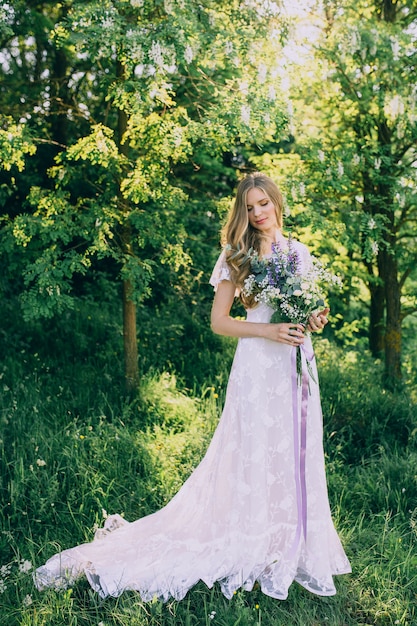 Moça em um vestido branco no prado. Mulher em um lindo vestido longo posando no jardim