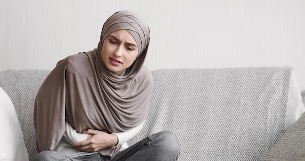 Moça muçulmana doente de hijab com dor abdominal aguda em casa