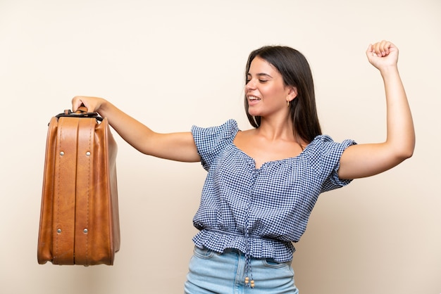 Moça sobre parede isolada, segurando uma maleta vintage