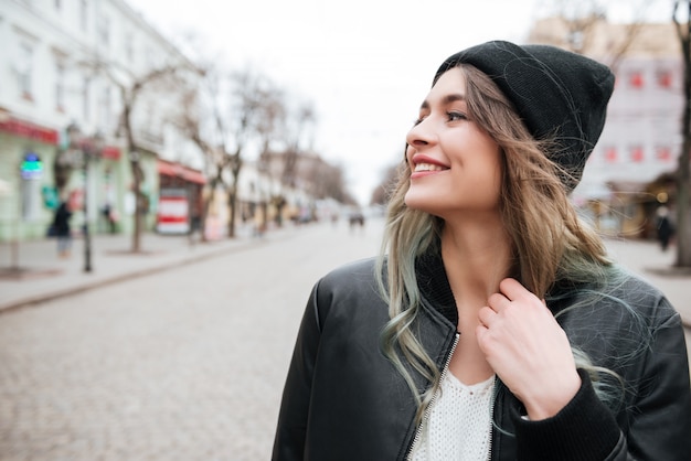 Moça sorridente usando chapéu andando na rua