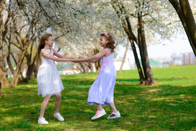 Moças bonitas com olhos azuis nos vestidos brancos no jardim com as macieiras que florescem se divertindo e apreciando o cheiro do jardim primavera.