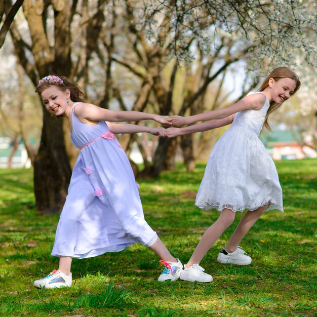 Moças bonitas com olhos azuis nos vestidos brancos no jardim com as macieiras que florescem se divertindo e apreciando o cheiro do jardim primavera.