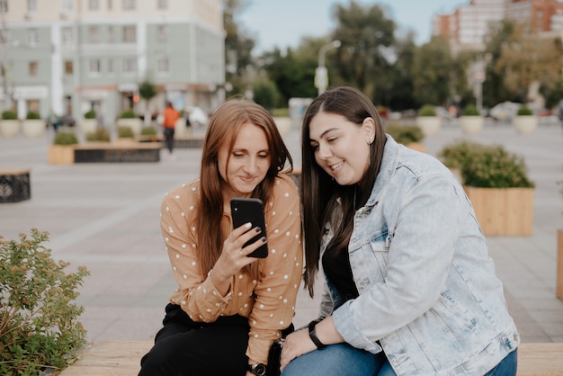 moças sentadas em um parque da cidade com um telefone