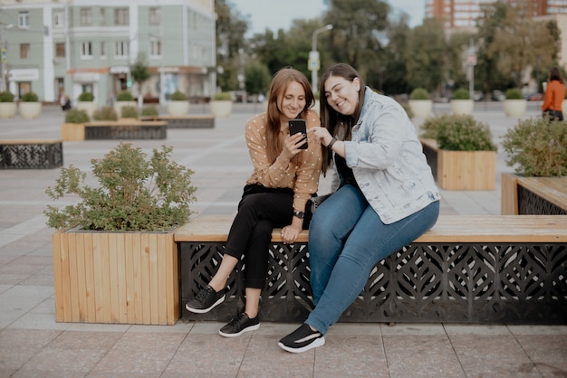 moças sentadas em um parque da cidade com um telefone