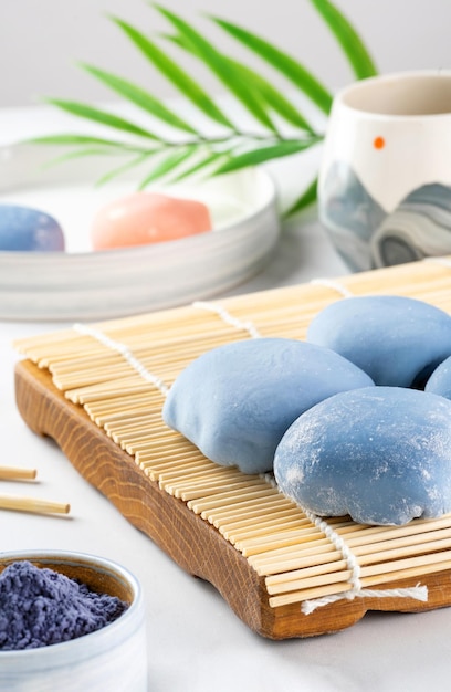 Un mochi japonés sobre una alfombra de madera sobre una encimera blanca Concepto de un postre japonés tradicional en la mesa de la cocina Pastel de arroz asiático con helado azul de matcha mochi Comida callejera dulce asiática