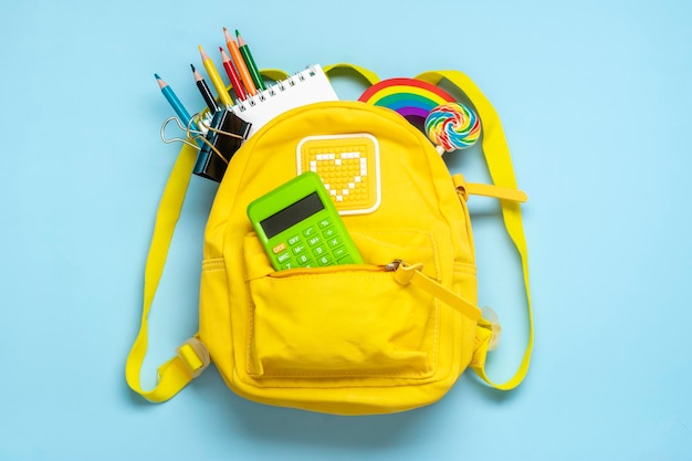 Foto mochila amarela com números de borracha de canetas de caderno de material escolar isolados em fundo azul