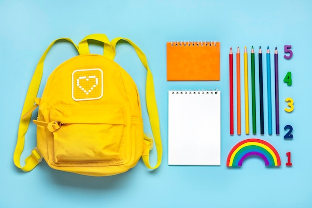 Foto mochila amarilla con útiles escolares cuaderno bolígrafos números de borrador aislado sobre fondo azul.