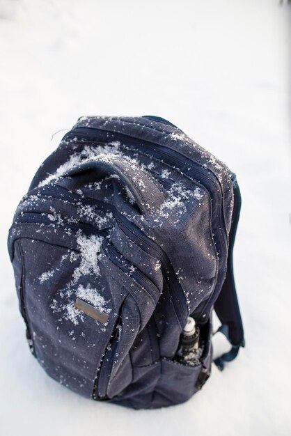 mochila azul com uma garrafa de água no bolso de pé em um dia nublado frio de neve