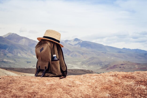 Mochila bege, garrafa de água e chapéu de palha na colina nas montanhas. Conceito de viagens ativas.