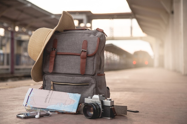 Foto mochila, celular, fone de ouvido, mapa, chapéu e filme de câmera no chão na estação de trem