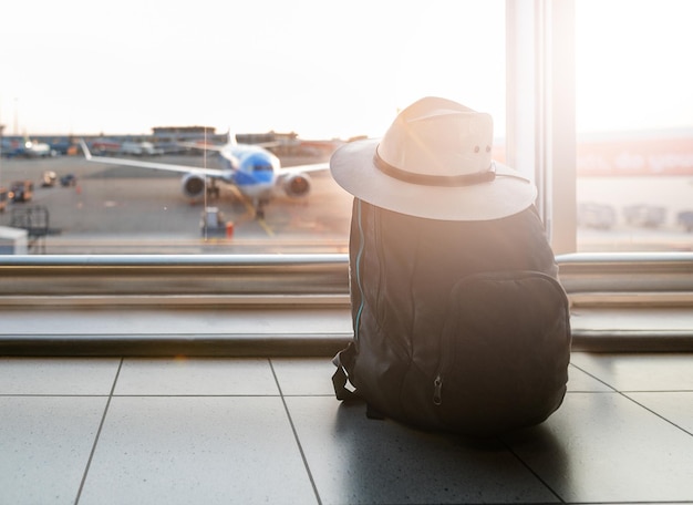 Foto mochila cerca de la ventana con el avión en el aeropuerto esperando en la sala de salida