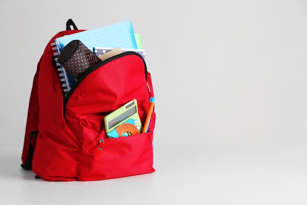 Mochila com suprimentos escolares em mesa de madeira