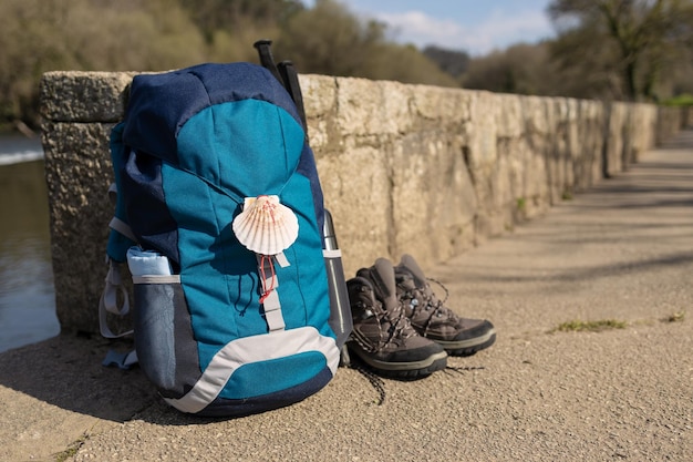 Foto mochila con concha de mar símbolo del camino de santiago botas de trekking y postes apoyados en la pared de piedra