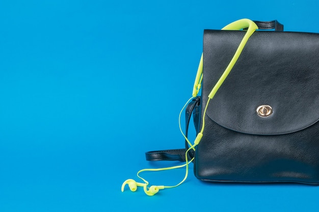 Mochila de cuero para mujer y auriculares amarillos sobre fondo azul. El concepto de turismo y educación.