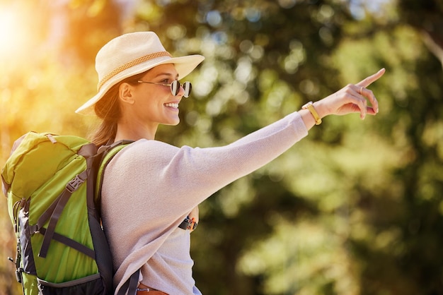 Mochila de mulher feliz ou apontando na natureza, viagem, parque de turismo ou aventura de observação de pássaros em árvores, floresta Sorriso, turista e direção, mão em local de caminhada, floresta do Canadá ou pesquisa de interface