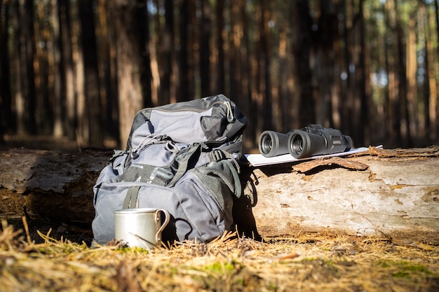 Mochila de turista, chapéu, binóculos e um mapa em um tronco na floresta. Caminhadas de conceito, caminhadas nas montanhas.