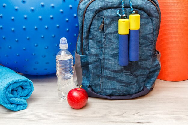 Foto mochila y diferentes herramientas para fitness en habitación o gimnasio en piso gris