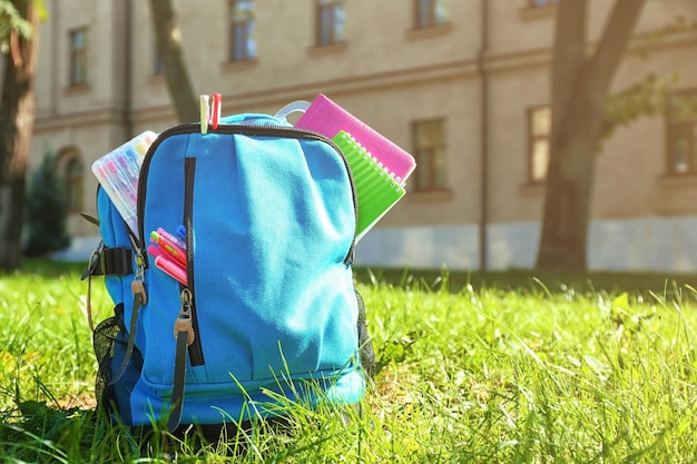 Mochila escolar con accesorios sobre hierba verde.