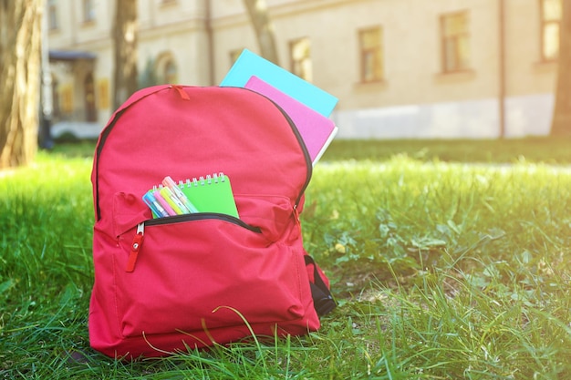 Mochila escolar con accesorios sobre hierba verde.