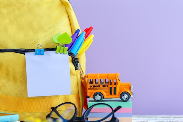 Mochila escolar amarela completa com artigos de papelaria na mesa em fundo roxo