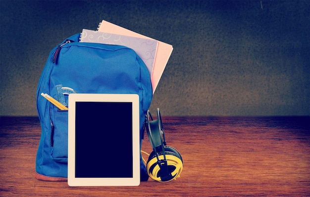 Foto mochila escolar azul com tablet e fones de ouvido no fundo da sala de aula