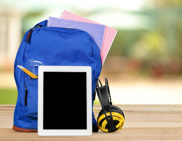 Foto mochila escolar azul com tablet e fones de ouvido no fundo da sala de aula