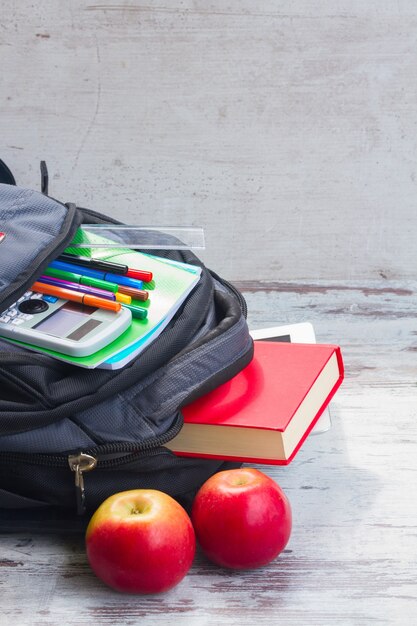 Mochila escolar com suprimentos e duas maçãs na mesa branca