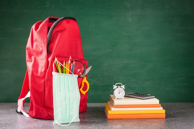 Mochila escolar frontal e acessórios com máscara facial protegem na mesa no quadro-negro