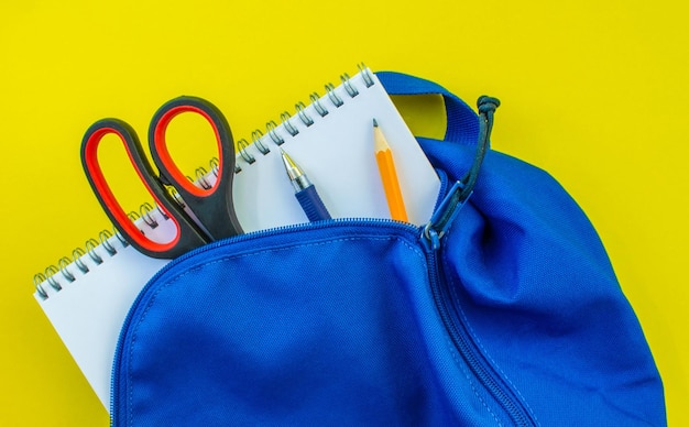 Mochila escolar lápiz pluma tijeras y bloc de notas sobre un fondo amarillo