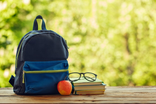 Mochila escolar con libros sobre fondo de naturaleza y mesa de madera