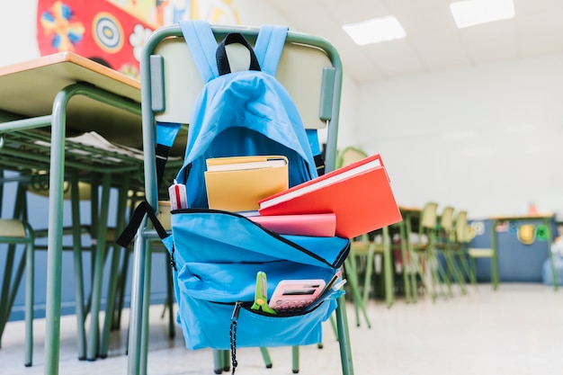 Foto mochila escolar con libros de texto en silla.